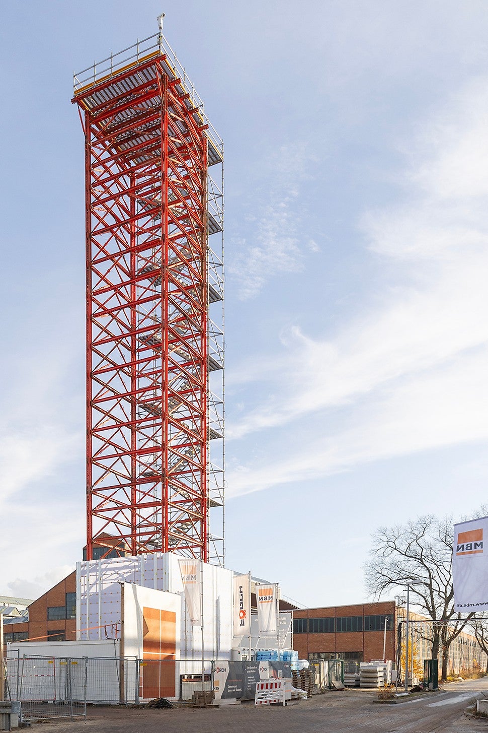 Der seitlich angebaute PERI UP Treppenturm mit 1,00 m Stufenbreite führt sicher und bequem bis zur Plattform in 30 m Höhe, während eine umlaufende Sockel-Einhausung mit PERI UP Cladding den Zugang zuverlässig abschottet.