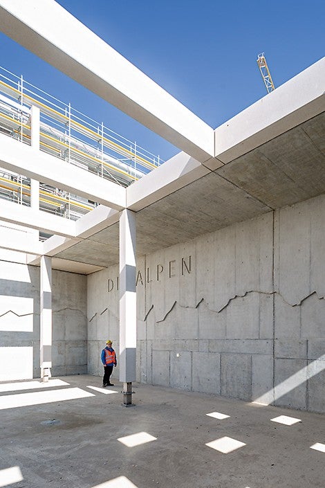 Velkoplošný betonový obraz panorama Alp ve dvoře základní školy s přesně zobrazenými vrcholky hor podle vyfrézované bednicí desky připravené v montážní dílně PERI. 