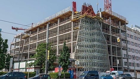 Atypický roh budovy ve tvaru sbíhající se lomené plochy - nakloněné stěny s bedněním MAXIMO, zapřeným rámy ze závor SRU a dílů VARIOKIT, postavené na nosné konstrukci z nosníků GT 24 a podpěrného lešení PERI UP Rosett.