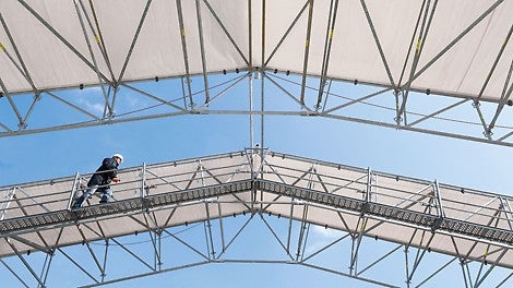 The proven PERI UP Rosett Flex LGS weather protection roof can now be supplemented with walkways for safe access. Suspended from the bottom chord, the brackets form – together with proven UDI decking and standard guardrails – safe walkways along the truss girder. Pre assembly takes place on the ground before the crane lifts the complete roof segment into position.