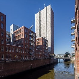 Das mit PERI UP eingerüstete Columbus Haus prägt die Silhouette der Hamburger Speicherstadt. Nur durch die Zustiegsöffnungen des Gerüstaufzugs hindurch sind die roten VARIOKIT Stahlträger der Auflagerkonstruktionen im 10-m-Abstand zu erkennen.
