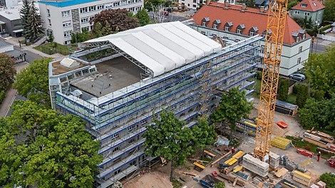 Zur Durchführung der aufwendigen Baumaßnahme muss die Gebäudesubstanz des Bestandsbauwerks während der gesamten Umbauphase gegen äußere Witterungseinflüsse geschützt werden.