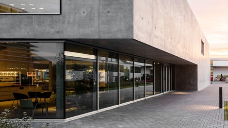 The canteen at the PERI headquarters in Weissenhorn was designed by the daughter of the company founder, architect Nathalie Schwörer, in collaboration with architects Mühlich, Fink &amp; Partner. Two cubes of almost equal size create a bright and open atmosphere. The southern cube made of exposed concrete houses the main entrance, the foyer with coffee bar and the kitchen. Glass is the dominant feature in the northern cube. This is where most of the seating is located, practically flowing into the outdoor area. Photo: Hiepler- Brunier Fotostudio esw