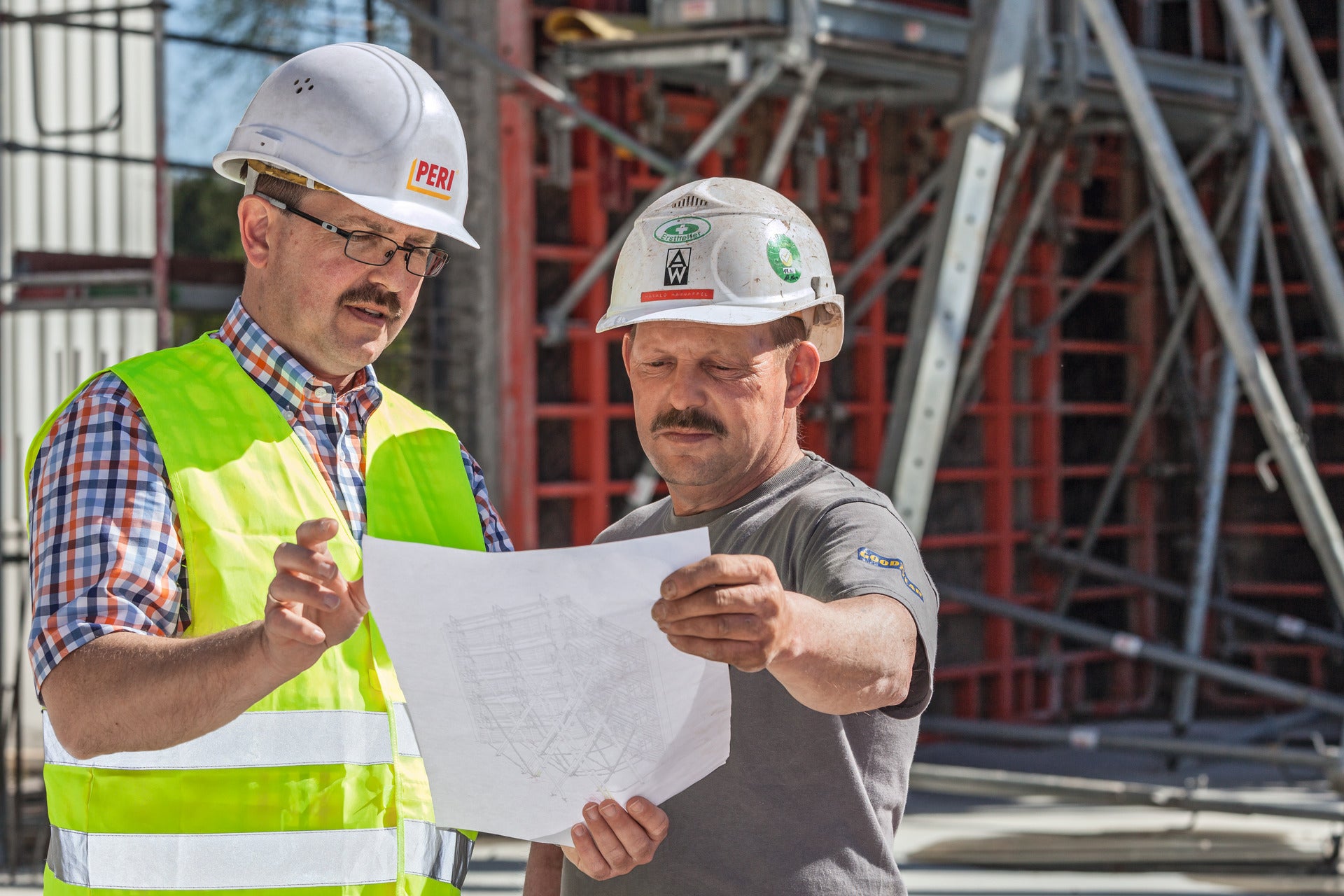 Bauleiter und Auftraggeber auf der Baustelle, beide schauen sich ein Dokument an